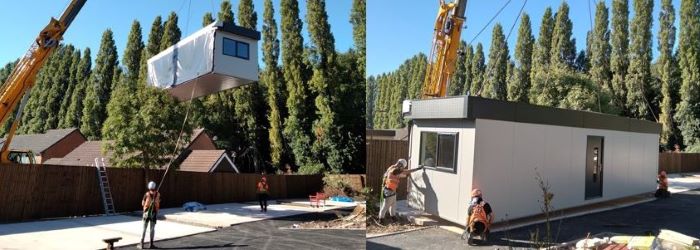 Modular building unit hoisted over perimeter fence by a crane 