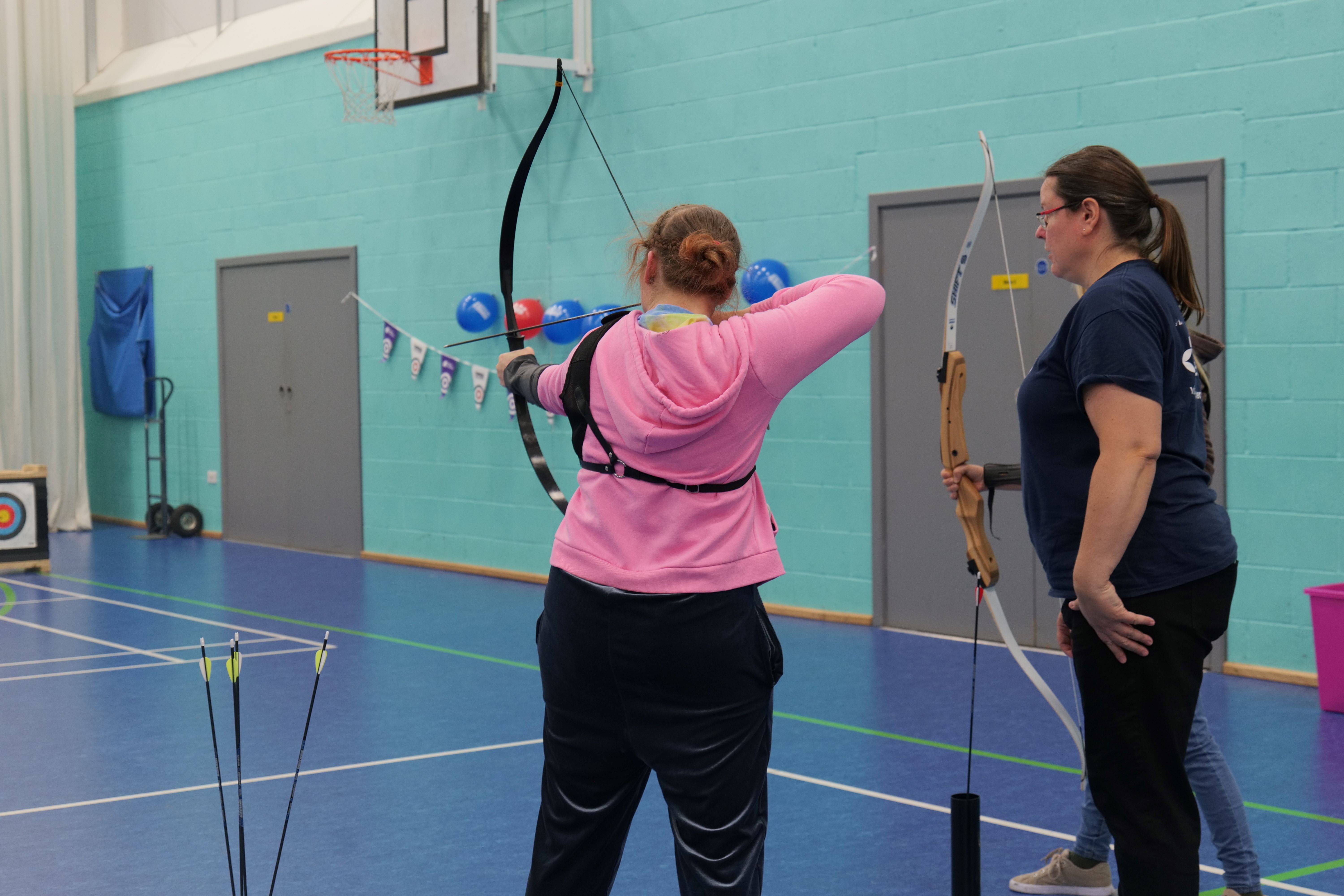 QAC student aiming a bow and arrow with GB archery staff watching