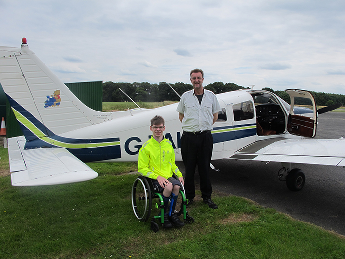 Bobby in wheelchair next to flight instructor, posing for photo in front of the plane