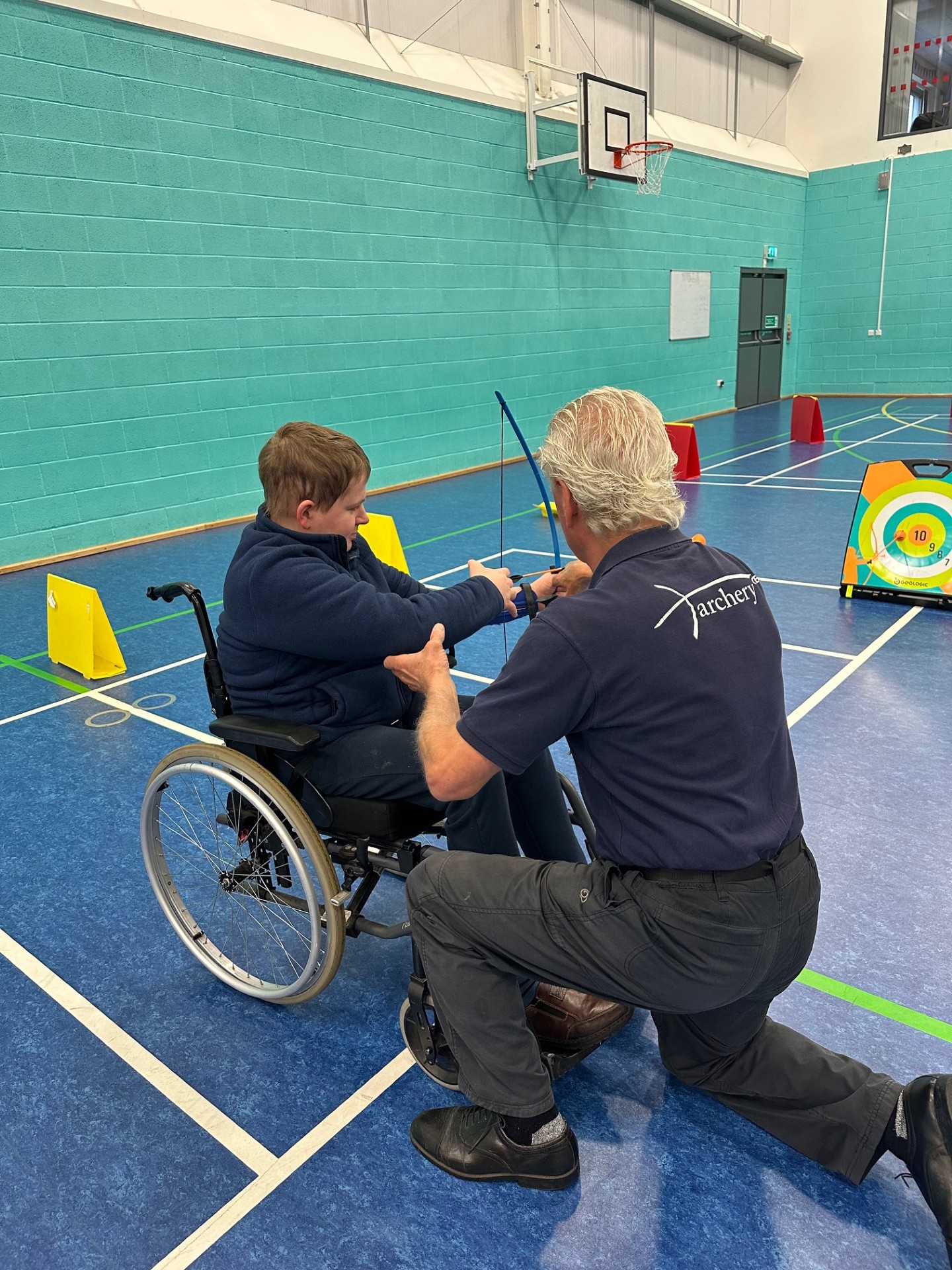 QAC Student Jack holding an archery set with assistance from Tony 