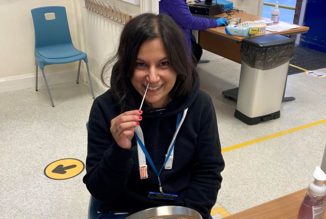 QAC staff member swabs inside the lining of her nostril in front of a mirror (friendly trained staff can provide help if needed)