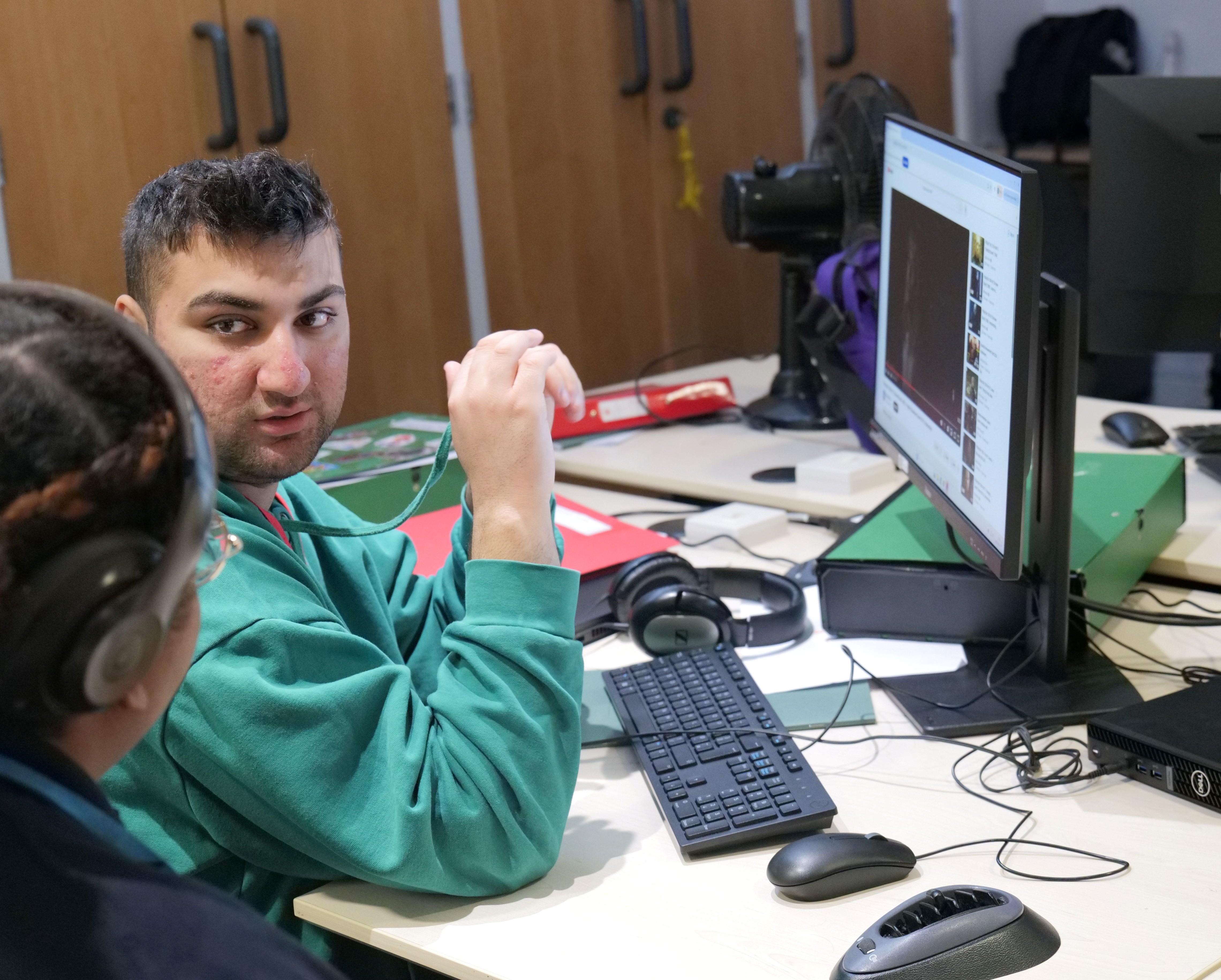 An image of a QAC student inside the Karten Centre using the desktop and talking to staff