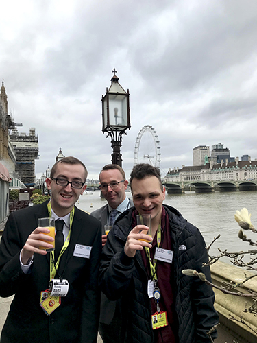 QAC Students Connor and Adam as well as Staff member Andy enjoying a drink outside the reception, with the London eye in the background