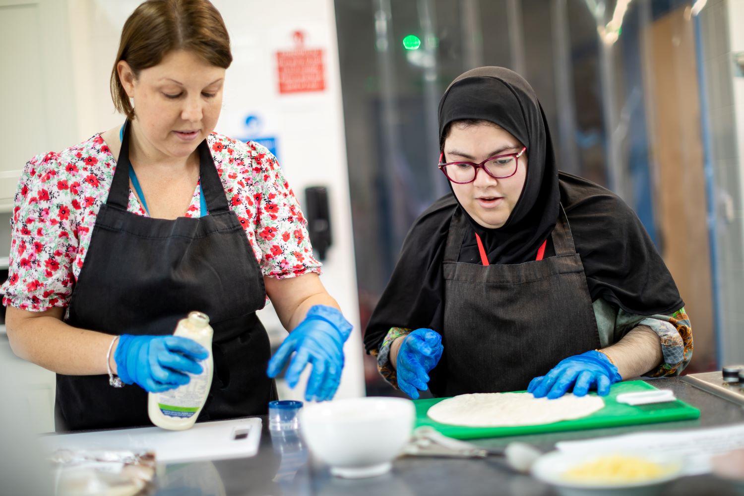 A student preps food in a café with a staff member supporting