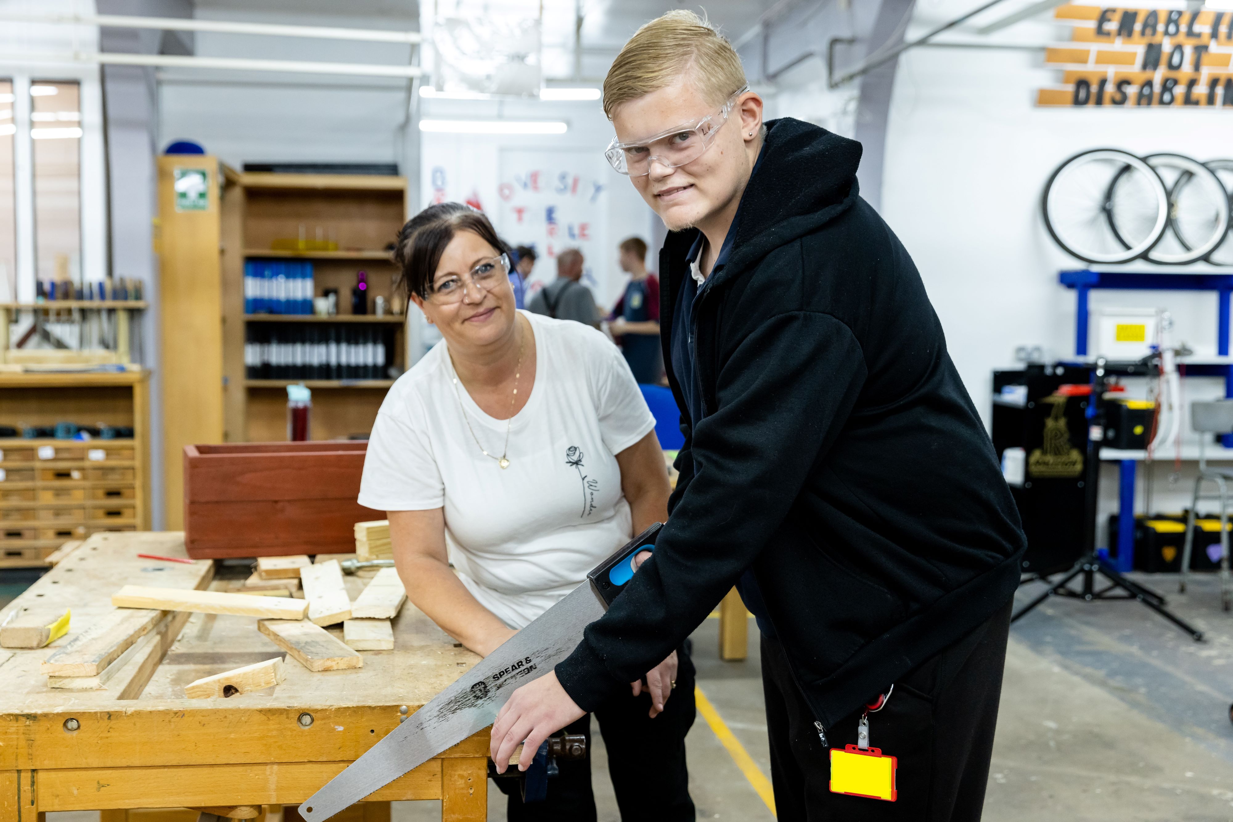 A student cuts wood with a workshop with a staff member supporting  