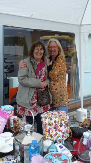 Two ladies behind a stall at the QAC Summer Fete, posing for a photo