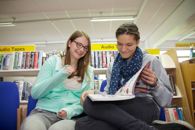 Two female students smile while looking at a book in the library